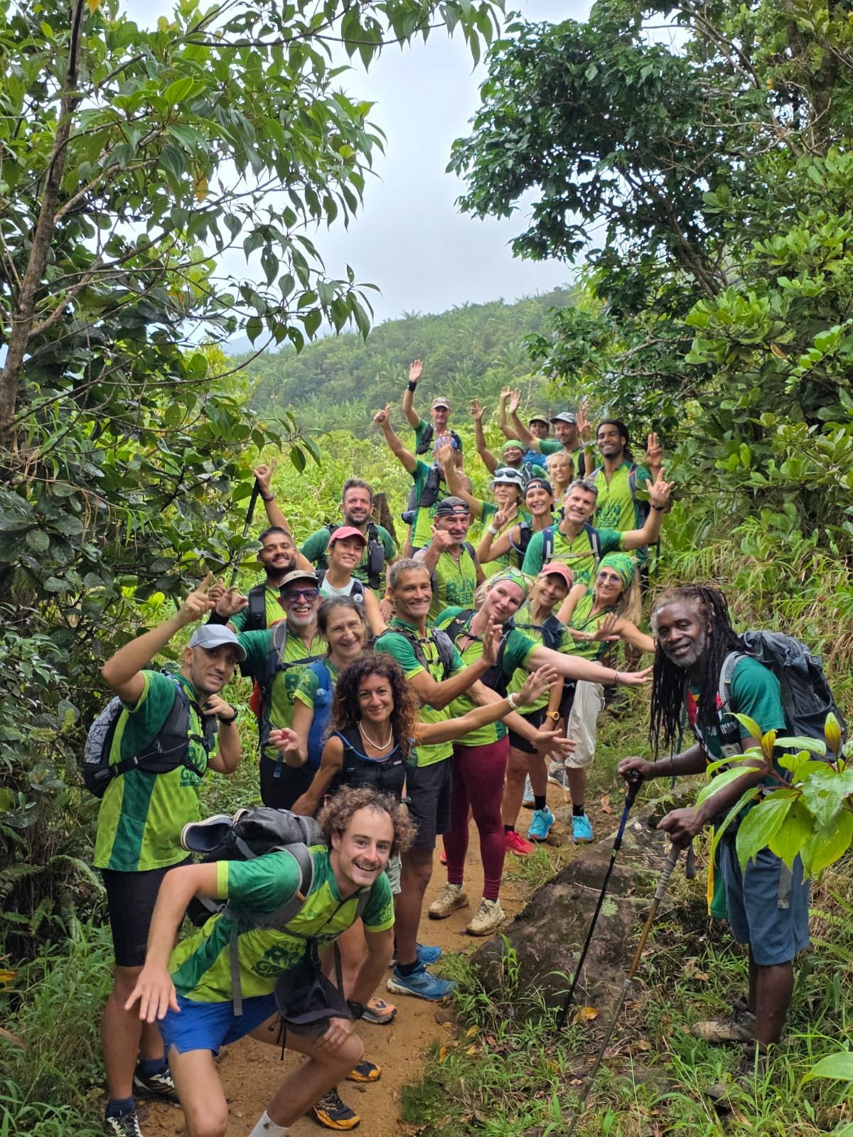Une vingtaine de membres de la Team Gwada Run Green, en maillot vert, sourient et saluent sur un sentier en forêt